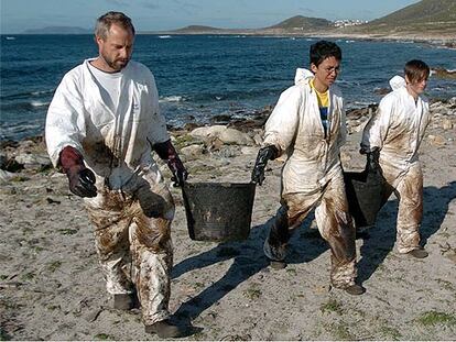 Tres voluntarios recogían ayer fuel incrustado en las rocas en la costa de Carnota (A Coruña).