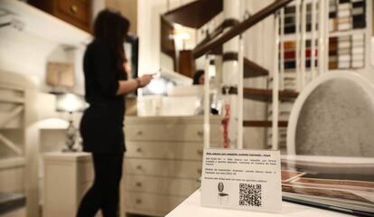 Una usuaria de la tienda de muebles sin dependientes observa la oferta. En primer plano, el código para acceder a la información del producto y comprar.
