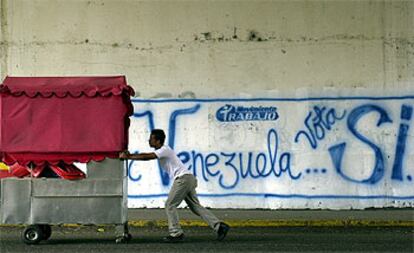 Un vendedor ambulante empuja su carrito en una calle de Caracas ante un mural que pide la revocación del presidente Chávez.