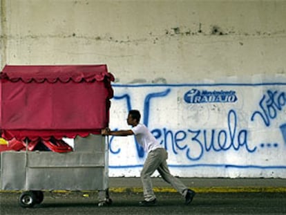 Un vendedor ambulante empuja su carrito en una calle de Caracas ante un mural que pide la revocación del presidente Chávez.