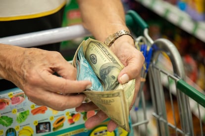O professor aposentado manuseia sua carteira enquanto faz compras.