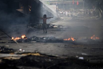 Un miembro de los <i>camisas rojas</i> camina a través del humo y el fuego en una calle céntrica de Bangkok.