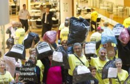 Afectados por participaciones preferentes y deuda subordinada de Novagalicia Banco se manifiestan esta mañana con bolsas de basura en la sede principal del banco en Vigo para simbolizar la devolución de los "productos tóxicos" que les "vendieron malamente" y reivindicar la vía del arbitraje "para todos".