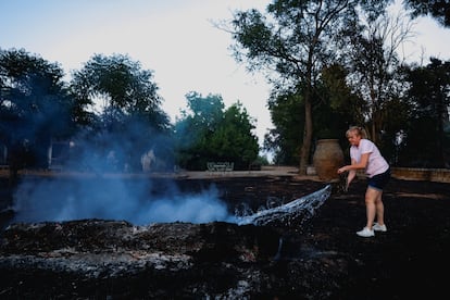 María Carmen Herráiz vierte agua para apagar el incendio en el jardín de su vivienda en Valmojado, este jueves.