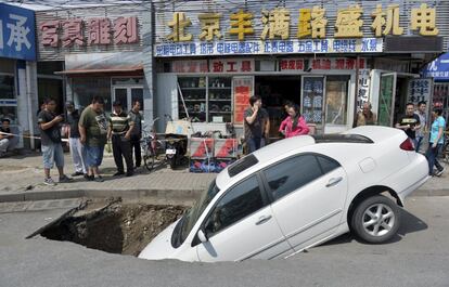 Transeúntes se paran a mirar el vehículo que ha quedado atrapado en un socavón en una calle en Pekín (China).