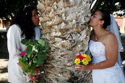 Dos mujeres vestidas con el tradicional vestido blanco de boda abrazan un árbol durante la ceremonia en la que participaron una veintena de vecinos.