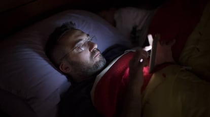 Un hombre lee a oscuras con su smartphone en la cama.