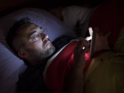 Un hombre lee a oscuras con su smartphone en la cama.