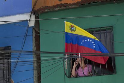 Una mujer se asoma a una ventana den la que ondea una bandera nacional venezolana para conmemorar el aniversario del fallecimiento de Hugo Chávez.