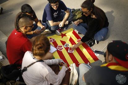 Un grupo de jóvenes juega a las cartas sobre una bandera independentista catalana antes del comienzo de la concentración.