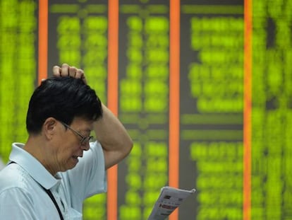 Un inversor llegeix un diari davant d'un panell amb cotitzacions a la Xina, on les caigudes es representen en verd.