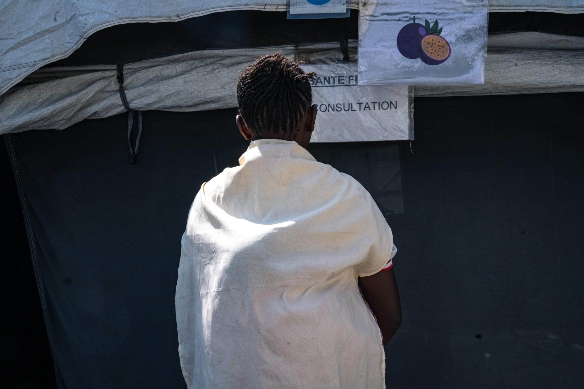 Foto de Laurianne con su bebé a cuestas frente a la sala de consultas en Goma en octubre de 2024.