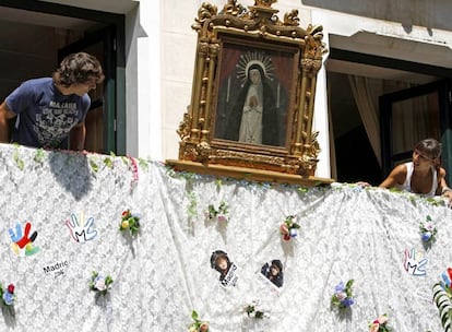 Un hombre y una mujer hablan en un balcón decorado con un lienzo de la Virgen de la Paloma.