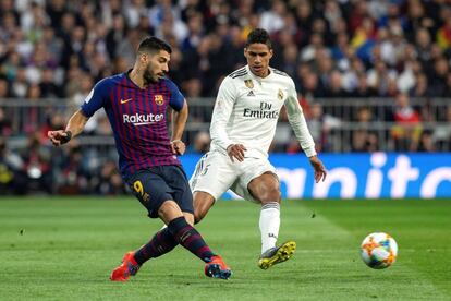 El delantero uruguayo del FC Barcelona Luis Suárez centra el balón presionado por el francés Raphael Varane, del Real Madrid.
