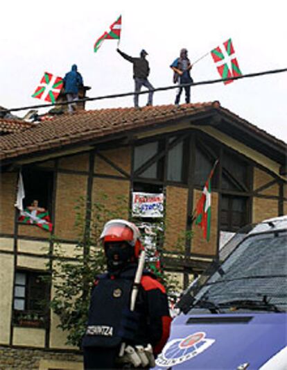 Un <i>ertzaina</i> vigila la <i>herriko taberna</i> de Durango, mientras partidarios de Batasuna permanecen en el tejado portando <i>ikurriñas.</i>