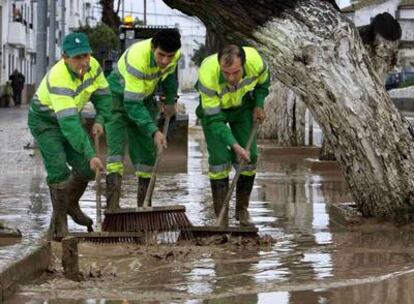 Empleados municipales de Lora del Río limpian ayer las calles de la localidad, anegadas por la crecida del Guadalquivir.