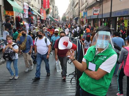 Un funcionario promueve el distanciamiento social en una concurrida calle comercial del centro histórico de la Ciudad de México.