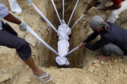 Varias personas introducen el cuerpo de una fallecida por la covid-19 en un cementerio de Nueva Delhi (India).