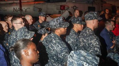 Tripulantes del portaviones, entre ellos una unidad de seguridad con uniformes de camuflaje, escuchan al capitán en el hangar del buque.
