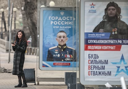 Una mujer espera el autobús en una parada con publicidad de reclutamiento militar en Moscú, Rusia, 19 de marzo de 2025