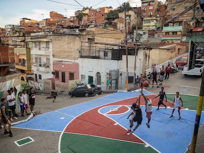 Niños y jóvenes juegan al baloncesto en una cancha restaurada por los vecinos en un barrio de Caracas.