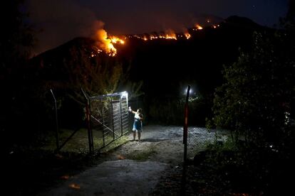 Una mujer cierra la puerta de una propiedad mientras el fuego hace estragos en una montaña cercana en Cajón del Maipo, en las afueras de Santiago de Chile (Chile).