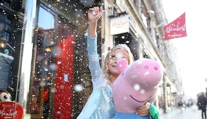 Una niña disfrazada de princesa sostiene un peluche de Peppa Pig.