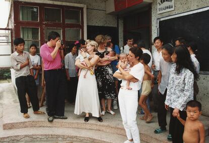 Seis familias belgas junto a los niños adoptados posan en la puerta del Centro Social de Acogida de Yueyang mientras los trabajadores y otros curiosos de la zona observan la escena, 1994.
