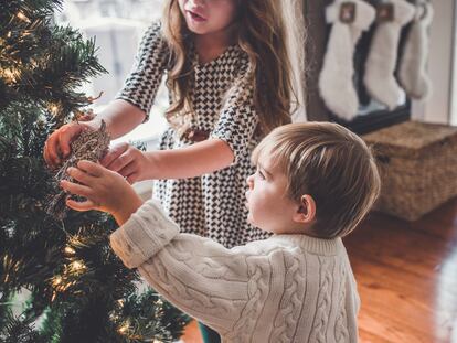 Dos hermanos decoran el árbol de Navidad.