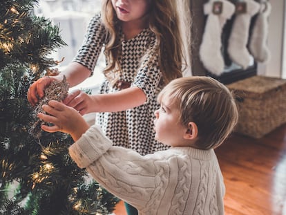 Dos hermanos decoran el árbol de Navidad.