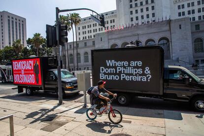 Un ciclista circula junto a dos camiones con mensajes sobre  la desaparición de Phillips y  Pereira, frente al Ayuntamiento de Los Ángeles, en California, el 8 de junio de 2022, en el marco de la IX Cumbre de las Américas.