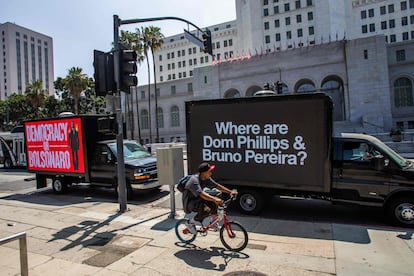 Un ciclista circula junto a dos camiones con mensajes sobre la desaparición de Phillips y Pereira, frente al Ayuntamiento de Los Ángeles, en California, el 8 de junio de 2022, en el marco de la IX Cumbre de las Américas.
