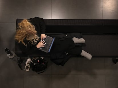 Una joven utiliza su ordenador tumbada en un sofá.