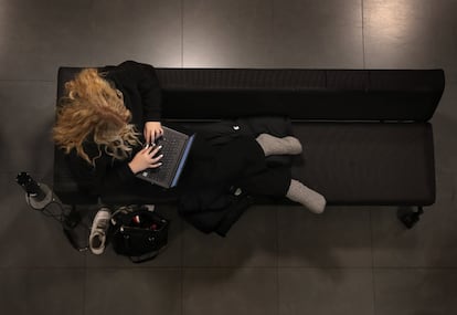 Una joven utiliza su ordenador tumbada en un sofá.