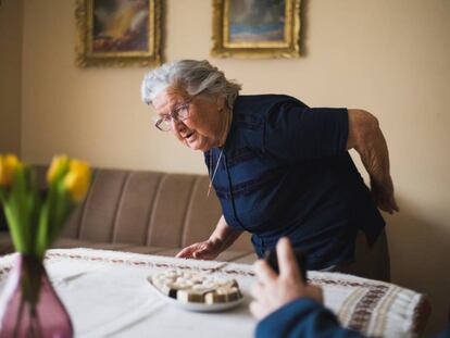 Mujer de edad avanzada de pie se toca la espalda con la mano. 