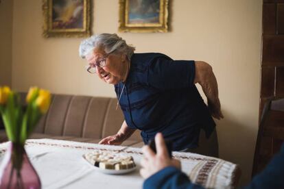 Mujer de edad avanzada de pie se toca la espalda con la mano.