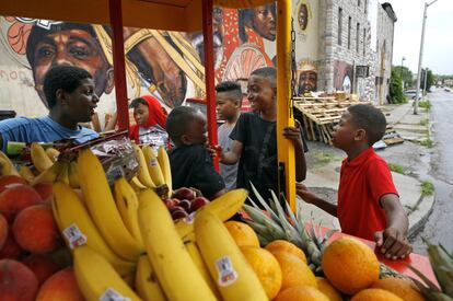 Unos niños se reúnen alrededor de un carro tirado por caballos lleno de comida a las afueras de un establo arabber en Baltimore. La tradición de jinetes urbanos conocidos como "arabbers" echó raíces en las familias negras de Baltimore después de la Guerra Civil y persiste en áreas donde la comida saludable es escasa.