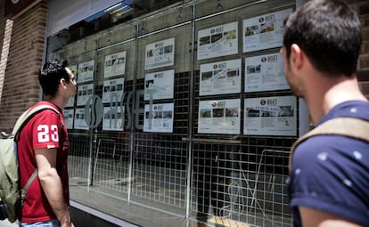 Dos personas observan el escaparate de una empresa inmobiliaria. 