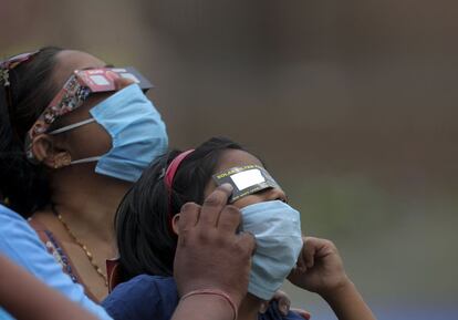 Dos mujeres observan el eclipse solar con gafas y mascarillas, en la ciudad india de Hyderabad.