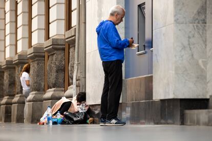 Un hombre saca dinero en un cajero de Gran Canaria, al lado de una persona sin hogar.