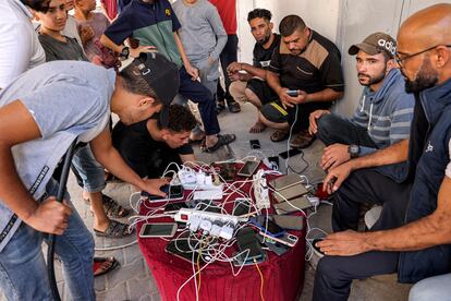 Varios hombres palestinos cargan su móvil en una fuente común de electricidad, frente a una farmacia cerrada en Rafah, este viernes.