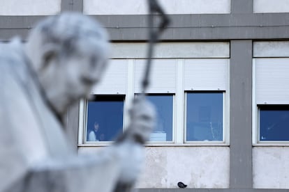 Varias personas cerca de una ventana en el Hospital Gemelli de Roma, este jueves. En primer término, la estatua del papa Juan Pablo II.