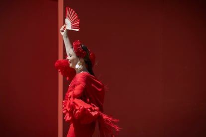 Una mujer vestida de flamenca saluda con el abanico al pasar bajo la portada.