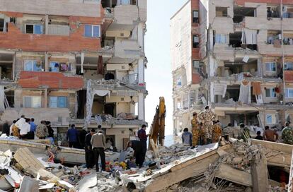 Personas de rescate buscan supervivientes junto a varios soldados iranís permanecen junto a edificios dañados en la ciudad de Pole-Zahab (Irán).