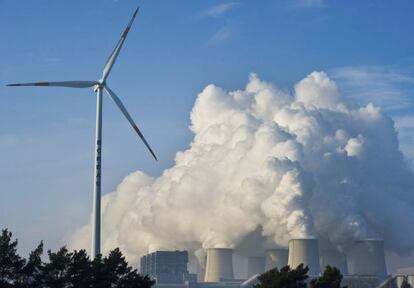 Uma turbina de energia e&oacute;lica em frente a uma usina. 