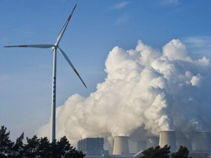 Uma turbina de energia e&oacute;lica em frente a uma usina. 