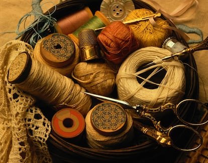 Bobinas, tijera, ovillos y otros objetos para coser en un costurero.