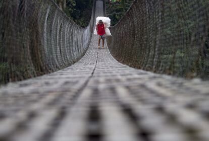 -FOTODELDIA- DH01 DHADING (NEPAL), 13/04/2015.- Un grangero nepalí traslada un fardo que contiene productos agrícolas mientras cruza una pasarela sobre el río Trishul en Nepal, hoy, 13 de abril de 2015. Granjeros nepalíes de la región atraviesan este puente colgante para abastecer con sus productos a los mercados de la zona. EFE/NARENDRA SHRESTHA