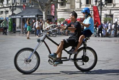 Dos jóvenes pasean por la plaza con una bicicleta customizada.