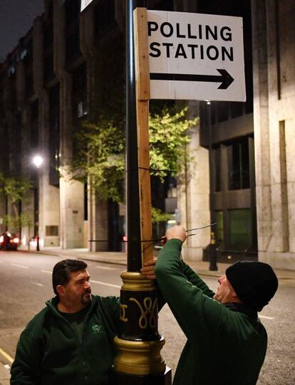 Dos trabajadores colocan carteles informando de la situación de los colegios electorales en el centro de Londres, este jueves.